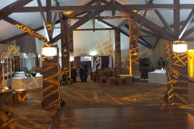 Salle de réception avec poutres apparentes, éclairage chaleureux et tables dressées en arrière-plan.