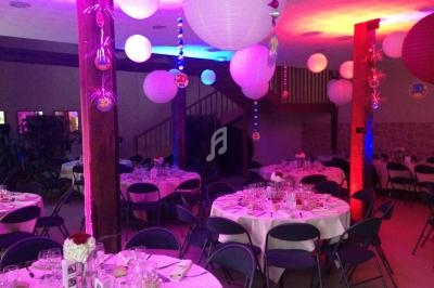Salle décorée pour un événement, avec des tables rondes dressées et des lanternes suspendues colorées.