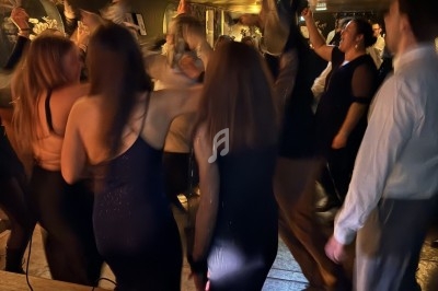 Groupe de personnes dansant dans une ambiance festive, éclairage tamisé, vue partielle d'une table de mixage au premier plan.