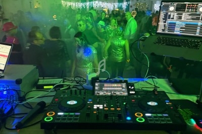 Vue depuis une table de mixage sur une piste de danse animée, éclairée par des lumières colorées et une ambiance festive.