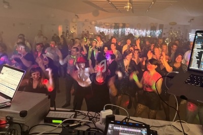 Vue depuis une table de mixage sur une foule dansante dans une salle éclairée par des lumières colorées.