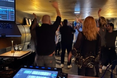 Groupe de personnes dansant dans un bar ou une salle avec une table de mixage au premier plan.