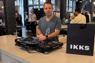 Un DJ mixe de la musique sur une table de mixage dans un magasin, avec un sac IKKS posé sur le comptoir.