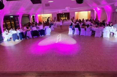 Salle de réception illuminée en rose avec des invités assis à des tables rondes pour un événement festif.
