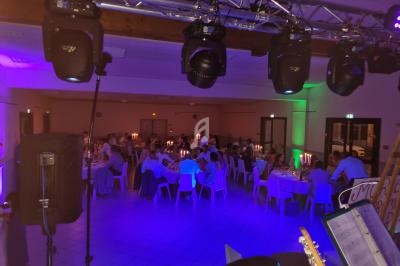 Salle de réception éclairée avec des invités assis à des tables rondes, ambiance tamisée et éclairages colorés.