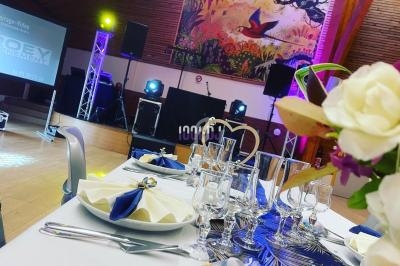 Salle de réception décorée avec une table dressée, des lumières colorées et une scène équipée pour un événement.
