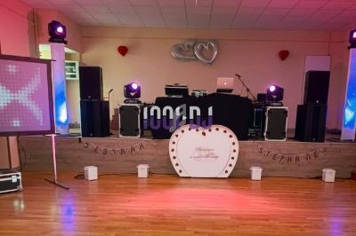 Salle décorée pour un événement avec piste de danse, éclairages colorés, écran, et arche de ballons rouges et argentés.