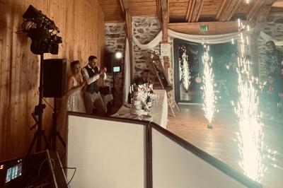 Un couple de mariés applaudit près d'une table avec un gâteau, entouré de décorations et de jets de lumière.