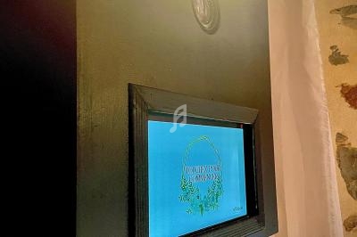 Borne photo avec écran tactile allumé, éclairée par une lampe, devant un mur en pierre.