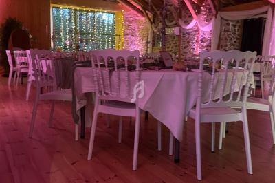 Salle de réception décorée avec des tables dressées, des chaises blanches et un éclairage tamisé rose.