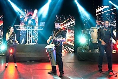 Des musiciens et chanteurs se produisent sur scène avec des lumières colorées et des écrans en arrière-plan.