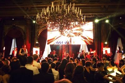 Salle de réception avec un groupe de musique jouant sur scène, éclairages vifs et invités dansant.