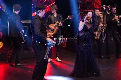 Un groupe de musiciens et une chanteuse se produisent sur scène avec des éclairages rouges et noirs.