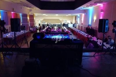 Salle de réception éclairée avec des tables dressées, vue depuis une scène équipée de matériel de sonorisation.