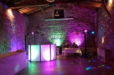 Salle en pierre éclairée par des lumières colorées, avec une table de DJ et deux personnes assises à une table.