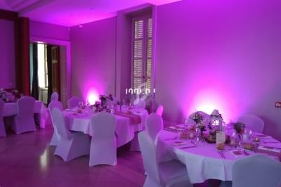 Salle de réception décorée avec des tables rondes, nappes blanches et éclairage d'ambiance rose.