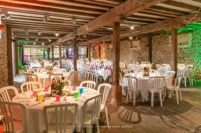 Salle de réception rustique avec tables rondes décorées, chaises blanches et murs en pierre apparente.