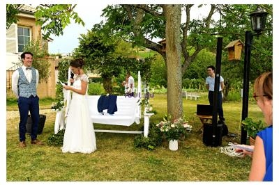 Un couple se tient près d'une balançoire blanche lors d'une cérémonie en extérieur, entouré de verdure et de décorations…