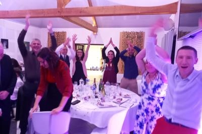 Des personnes debout autour de tables décorées, levant les bras dans une ambiance festive à l'intérieur d'une salle.