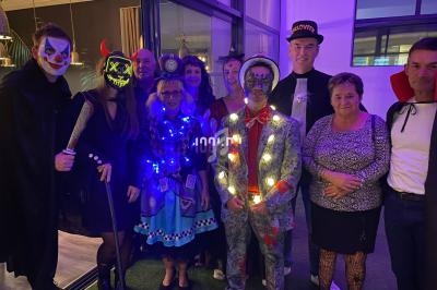 Un groupe de personnes déguisées pour Halloween, avec des costumes lumineux et des accessoires variés, posant dans une salle.