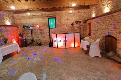 Salle en pierre avec éclairage coloré, tables décorées et espace aménagé pour une animation musicale.