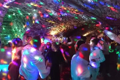 Personnes dansant sous des lumières colorées dans une salle voûtée en pierre.