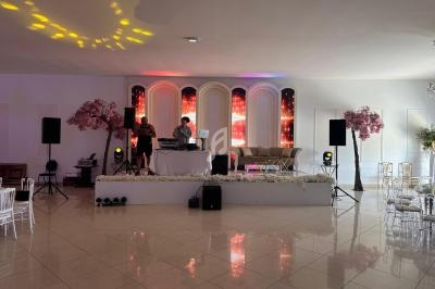 Scène avec deux DJ, éclairage coloré, décor floral et mobilier élégant dans une salle lumineuse.