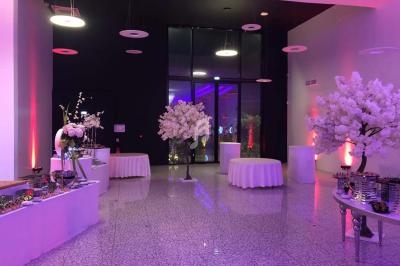 Salle de réception décorée avec des tables rondes drapées de blanc, des arbres artificiels et un éclairage coloré.