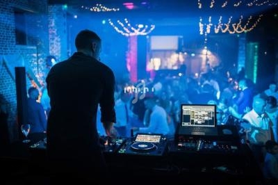Un DJ mixe de la musique sur une scène éclairée, face à une foule dansante dans une ambiance de club nocturne.