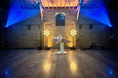 Salle en briques avec un éclairage coloré, projecteurs circulaires et un pupitre central sur un sol en marbre.