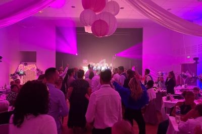 Des invités dansent sous des lumières colorées dans une salle décorée pour une fête ou un mariage.