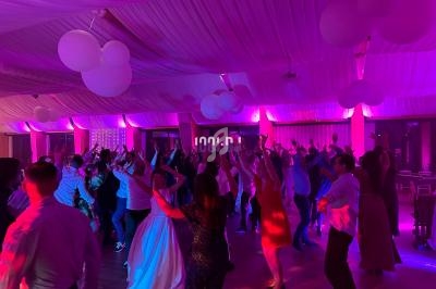 Des invités dansent sous une lumière colorée dans une salle décorée de ballons et de drapés suspendus.