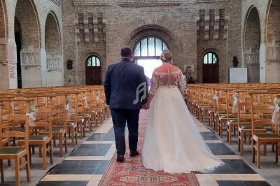 Un couple en tenue de mariage marche dans l'allée centrale d'une église lumineuse et spacieuse.