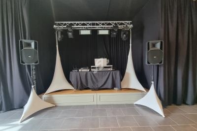 Scène avec une table de mixage, un ordinateur portable, des enceintes et des éclairages, entourée de rideaux noirs.