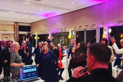 Groupe de personnes dansant et chantant lors d'une soirée festive dans une salle éclairée par des lumières colorées.