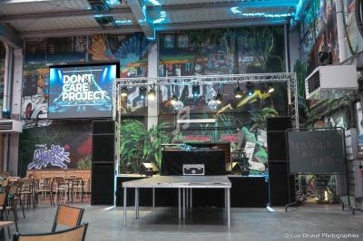 Scène de concert vide dans un espace industriel décoré de graffitis, avec des tables et chaises disposées autour.