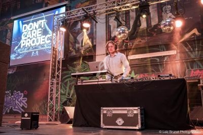 Un DJ mixe sur scène avec un ordinateur portable, entouré de matériel audio et éclairé par des projecteurs.