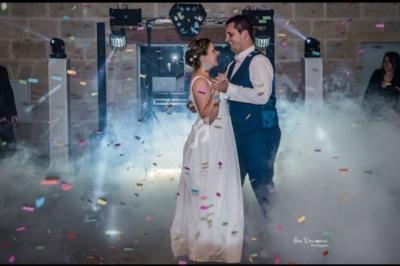 Un couple danse au milieu de confettis colorés et de fumée dans une salle décorée pour une fête.
