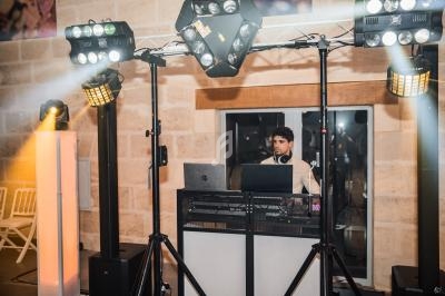 Un DJ mixe derrière une table équipée d'ordinateurs et de matériel audio, entouré de projecteurs lumineux.