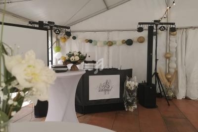 Table de mixage et décorations festives dans une tente blanche, avec guirlandes et fleurs en arrière-plan.