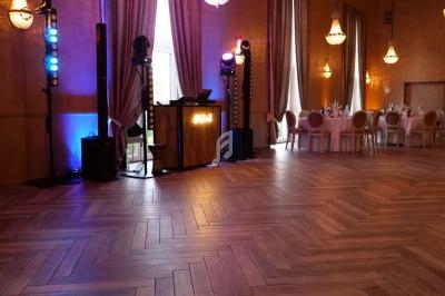 Salle de réception avec parquet en chevrons, tables dressées et espace réservé à un DJ avec éclairages colorés.