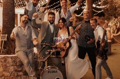 Un groupe de musiciens et une chanteuse posent joyeusement avec leurs instruments sous des guirlandes lumineuses.