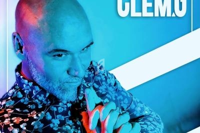 Homme chauve en chemise à motifs, posant avec les mains jointes dans une lumière bleue et rose.