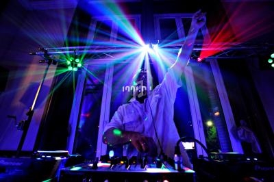 Un DJ mixant sur une scène éclairée par des faisceaux lumineux colorés dans une ambiance nocturne.