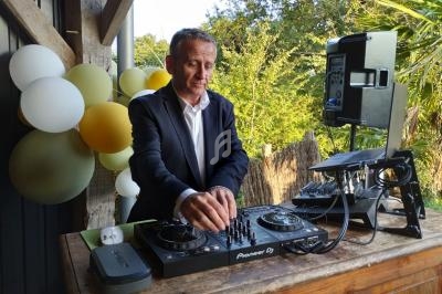 Un homme en costume utilise une table de mixage lors d'un événement en extérieur, avec des ballons en arrière-plan.