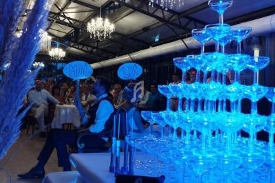 Pyramide de coupes à champagne illuminée en bleu dans une salle de réception avec des invités assis.