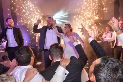 Un couple de mariés danse joyeusement entouré d'invités en tenue de soirée, avec des étincelles en arrière-plan.