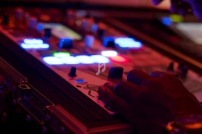 Main posée sur une console de mixage lumineuse avec des boutons et des voyants colorés dans un environnement sombre.