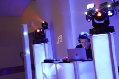 Un DJ mixe sur un ordinateur portable, entouré d'éclairages colorés dans une ambiance de soirée.