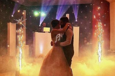 Un couple danse dans une ambiance festive avec éclairages colorés, fumée et étincelles décoratives.